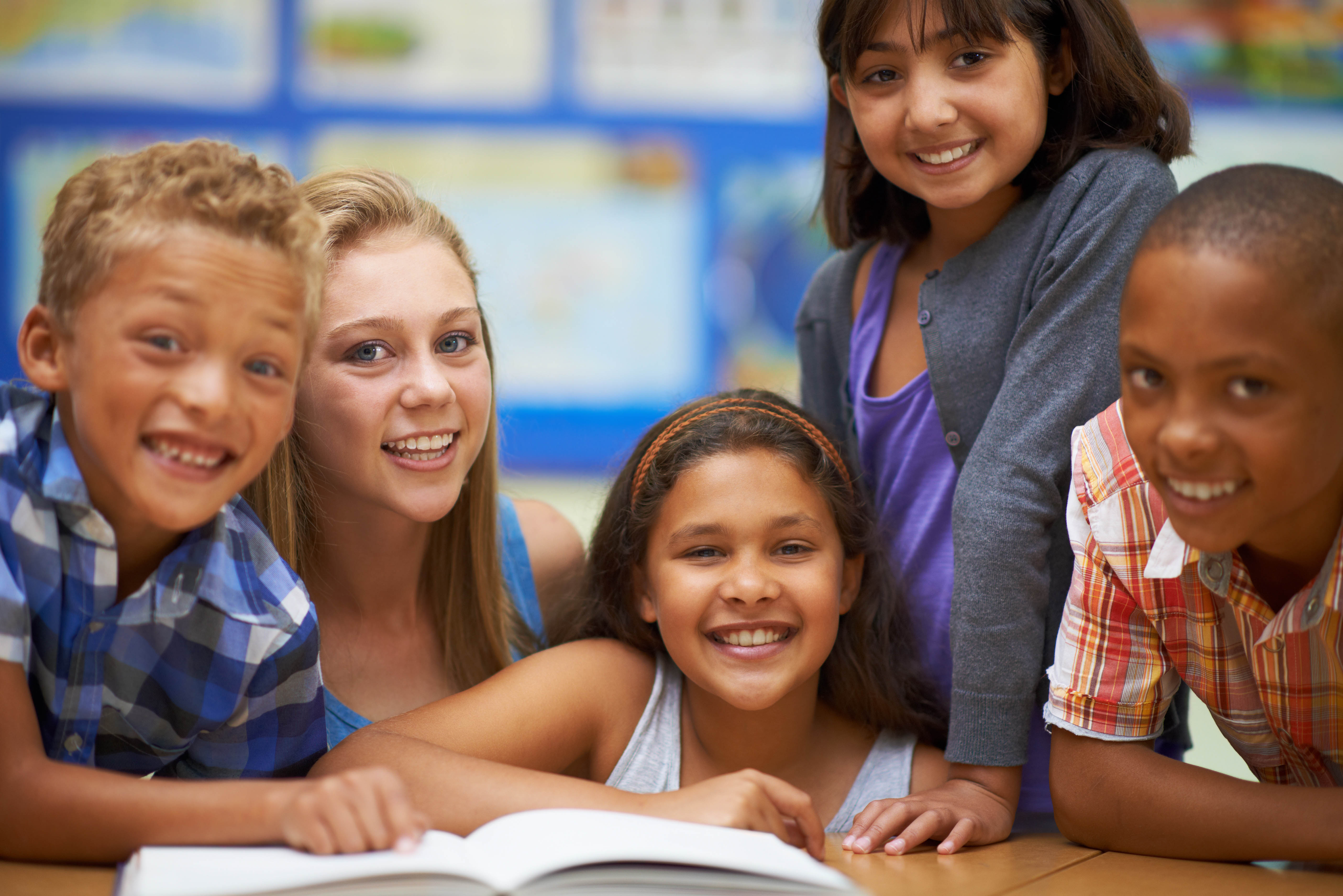 A diverse group of children gathered around a book in a classroom
