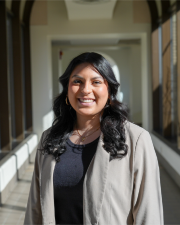 Gloria Gantt, a Hispanic woman with long, brown hair, wearing a black shirt grey overcoat.