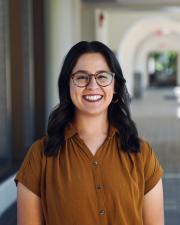 Kaela Bright, a woman with long, dark hair, wearing semi-circular glasses and a brown shirt