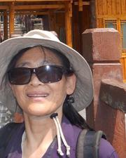 Joy Wu, an Asian-American woman in a purple shirt, wearing thick, square sunglasses and a white hat on her head.